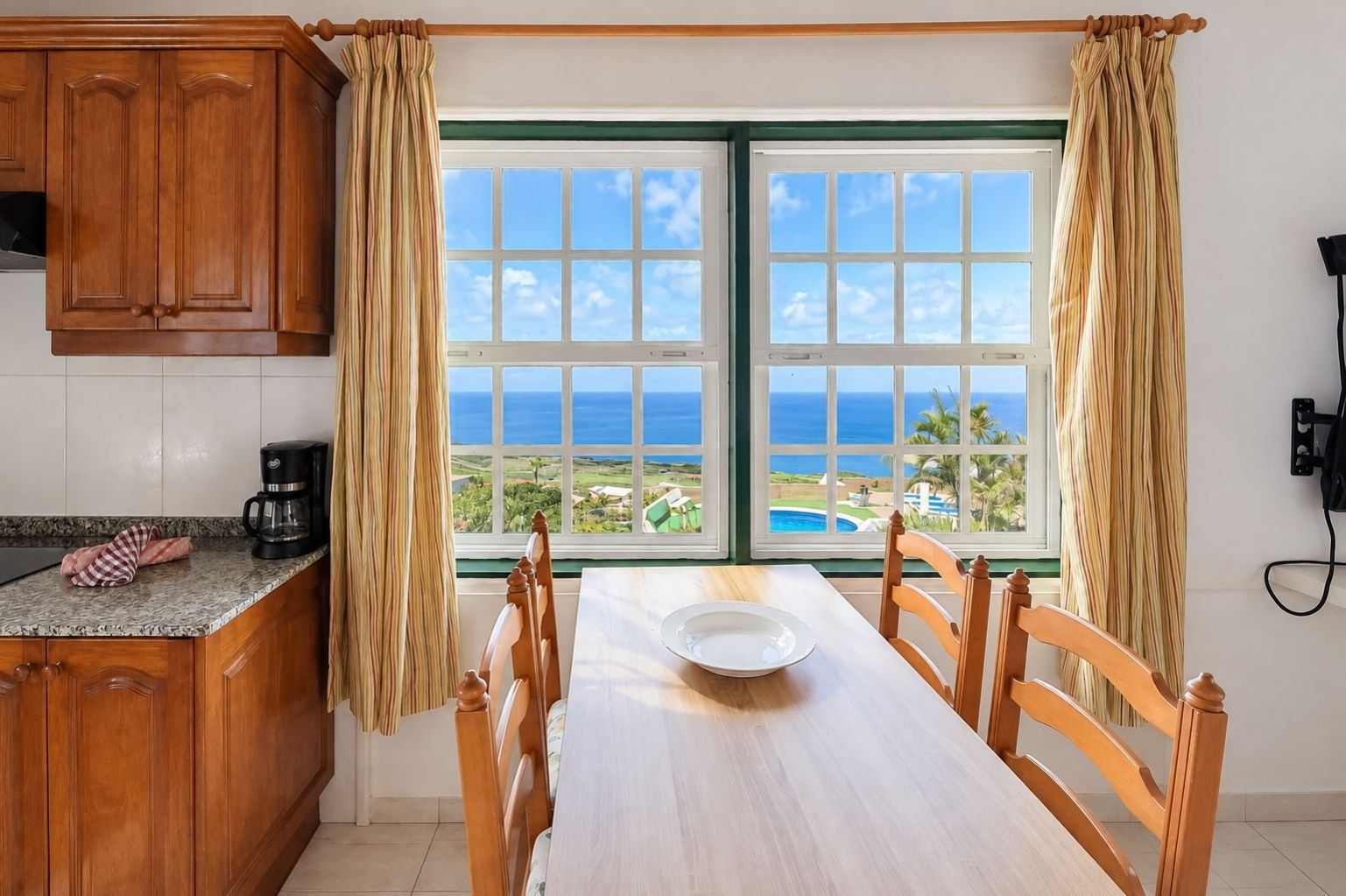 Comedor con vista al océano, muebles de madera y cafetera en la encimera.