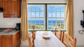 Comedor con vista al océano, muebles de madera y cafetera en la encimera.