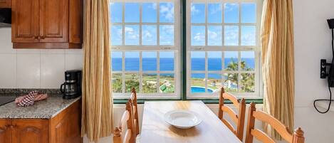 A dining area with a view of the ocean, wooden furniture, and a coffee maker on the counter.