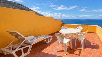 Una terraza con mesa y sillas, una tumbona y vista al mar.