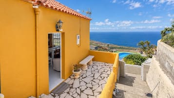 Un edificio amarillo con patio empedrado, piscina y vista al mar.
