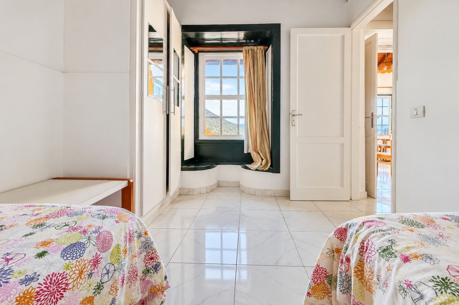 A hotel room with two beds, a window with curtains, a door, and a view of the outdoors.