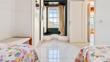 A hotel room with two beds, a window with curtains, a door, and a view of the outdoors.