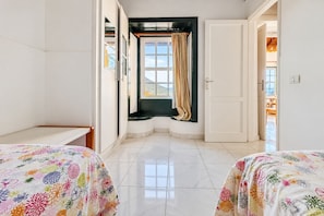 A hotel room with two beds, a window with curtains, a door, and a view of the outdoors. - GuestReady - Eva A 4 pax (Los Quemados)