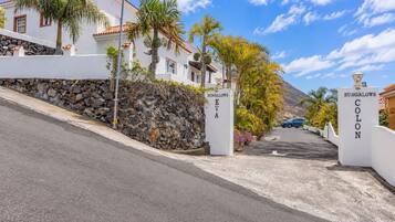 Una entrada protegida por una reja a una propiedad llamada 'BUNGALOWS EVA', con un muro de piedra y palmeras.