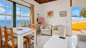 Ein Zimmer mit Esstisch, zwei Sofas, einem Fernseher und Blick auf den Ozean.