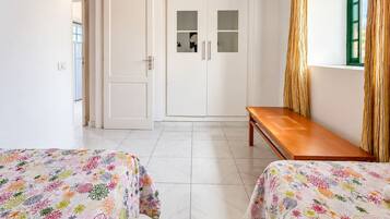 Una habitación con dos camas, un armario, un banco y una ventana con cortinas.