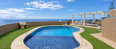 Piscina con vistas al océano, rodeada de césped artificial y sillas de descanso.