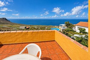 Un balcó amb vista a l'oceà, una piscina i una cadira blanca.