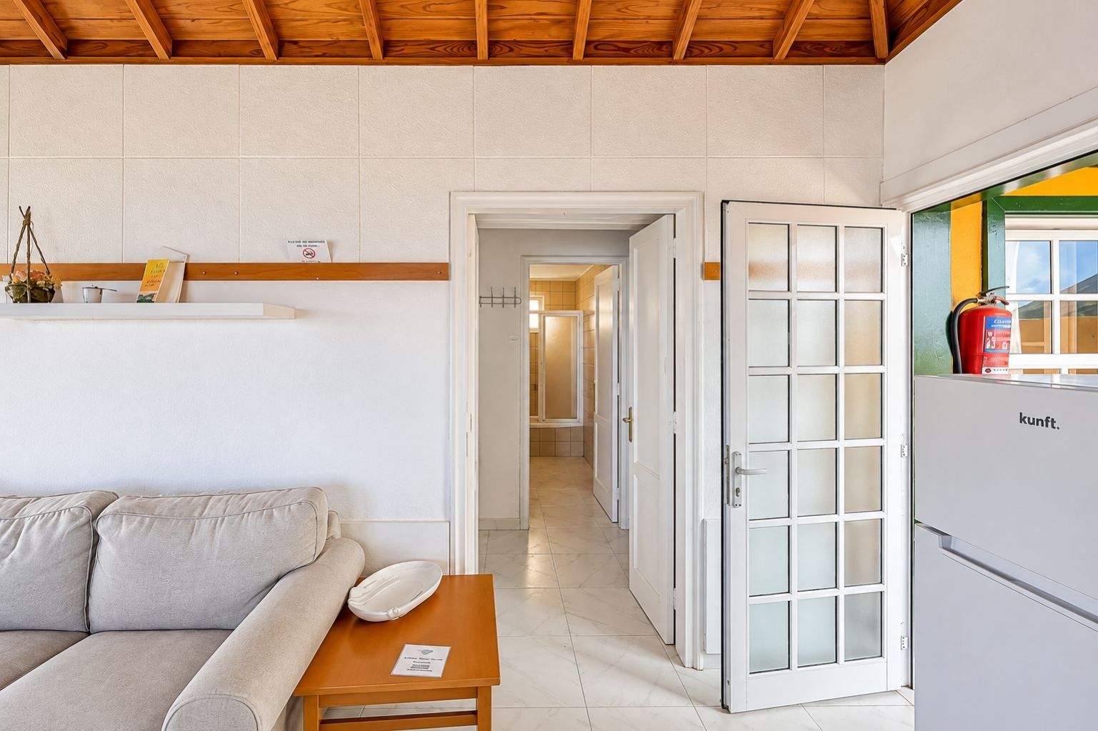 Una sala de estar con un sofá, una mesa y una puerta que da a un pasillo.