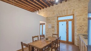 Un comedor con mesa y sillas de madera, paredes de piedra y una zona de cocina con pileta.