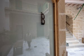 Eine Glastür mit dem Buchstaben 'B', die zu einer Steintreppe und einem Raum mit Fliesenboden führt.