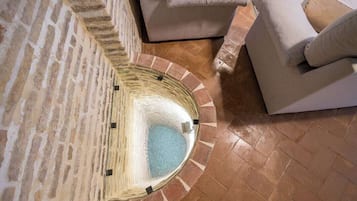 A stone-walled room with a circular water feature, a beige sofa, and a patterned floor.