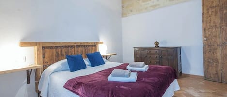 Quarto com cabeceira de madeira, cama com manta roxa, mesa de cabeceira de madeira e guarda-roupa.
