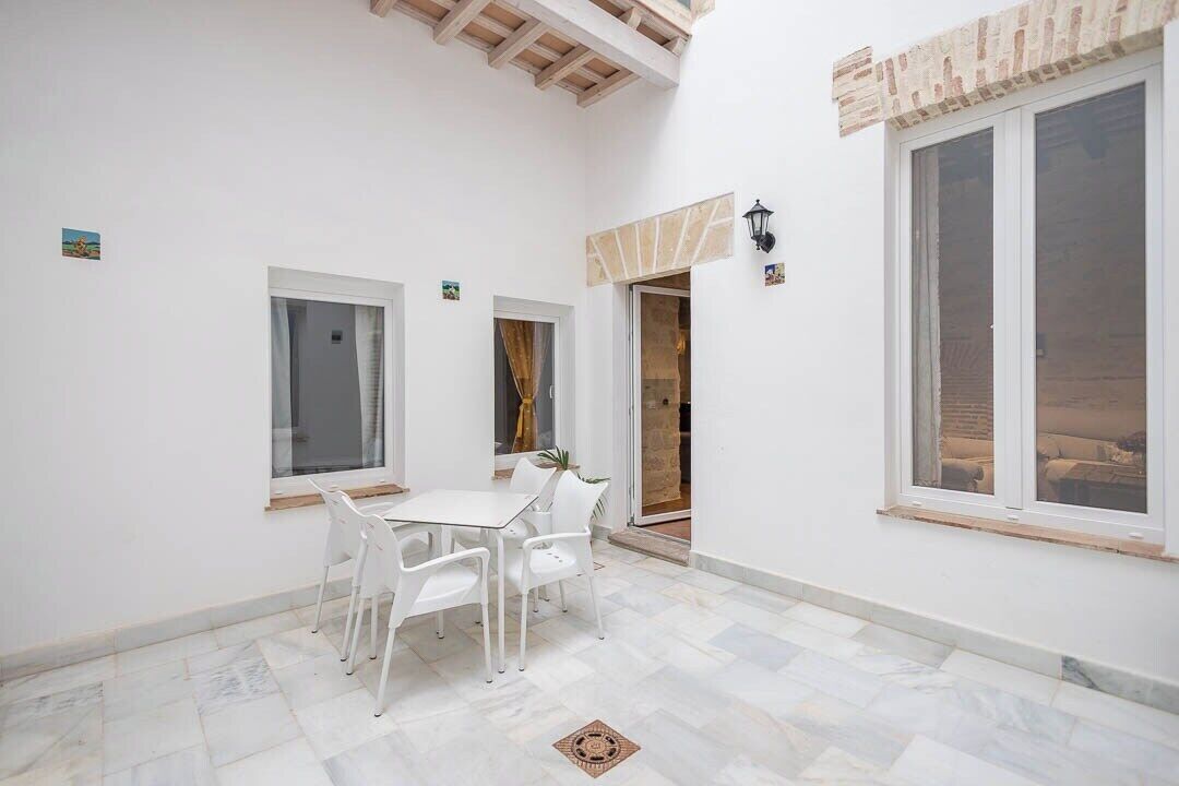 A room with a white table and chairs, a window, and a door leading outside.