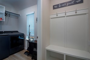Ein Waschraum mit Waschmaschine, Wäscheständer und Sitzbank. Eine Tür trägt ein Schild mit der Aufschrift 'seien Sie unser Gast'.