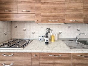 A kitchen with wooden cabinets, a gas stove, a sink, and a tiled backsplash. - Casa Mercò (Mercogliano)