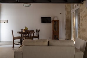 A living room with a sofa, a dining table with chairs, a TV mounted on the wall, and a cabinet. - GuestReady - La Cruz 2C (El Puerto de Santa María)