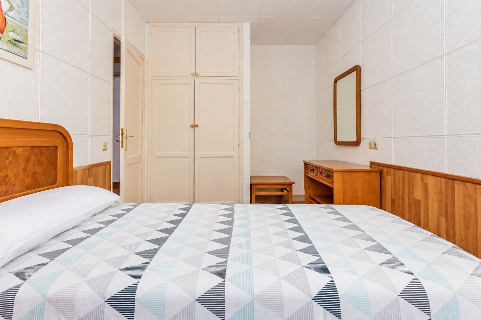 Un dormitorio con una cama, un aparador de madera, una mesita y un armario.