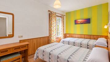 Una habitación con dos camas, un escritorio de madera, un espejo y una ventana con cortinas.