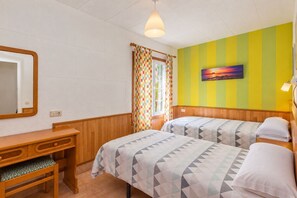 Una habitación con dos camas, un escritorio de madera, un espejo y una ventana con cortinas.