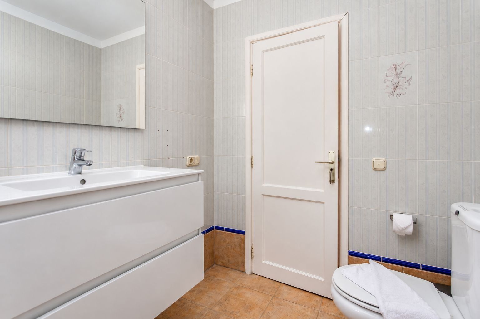 Une salle de bain avec un lavabo blanc, un miroir, une porte blanche et des toilettes.