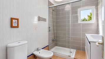 Un baño moderno con cabina de ducha de vidrio, inodoro, bidé y lavamanos.