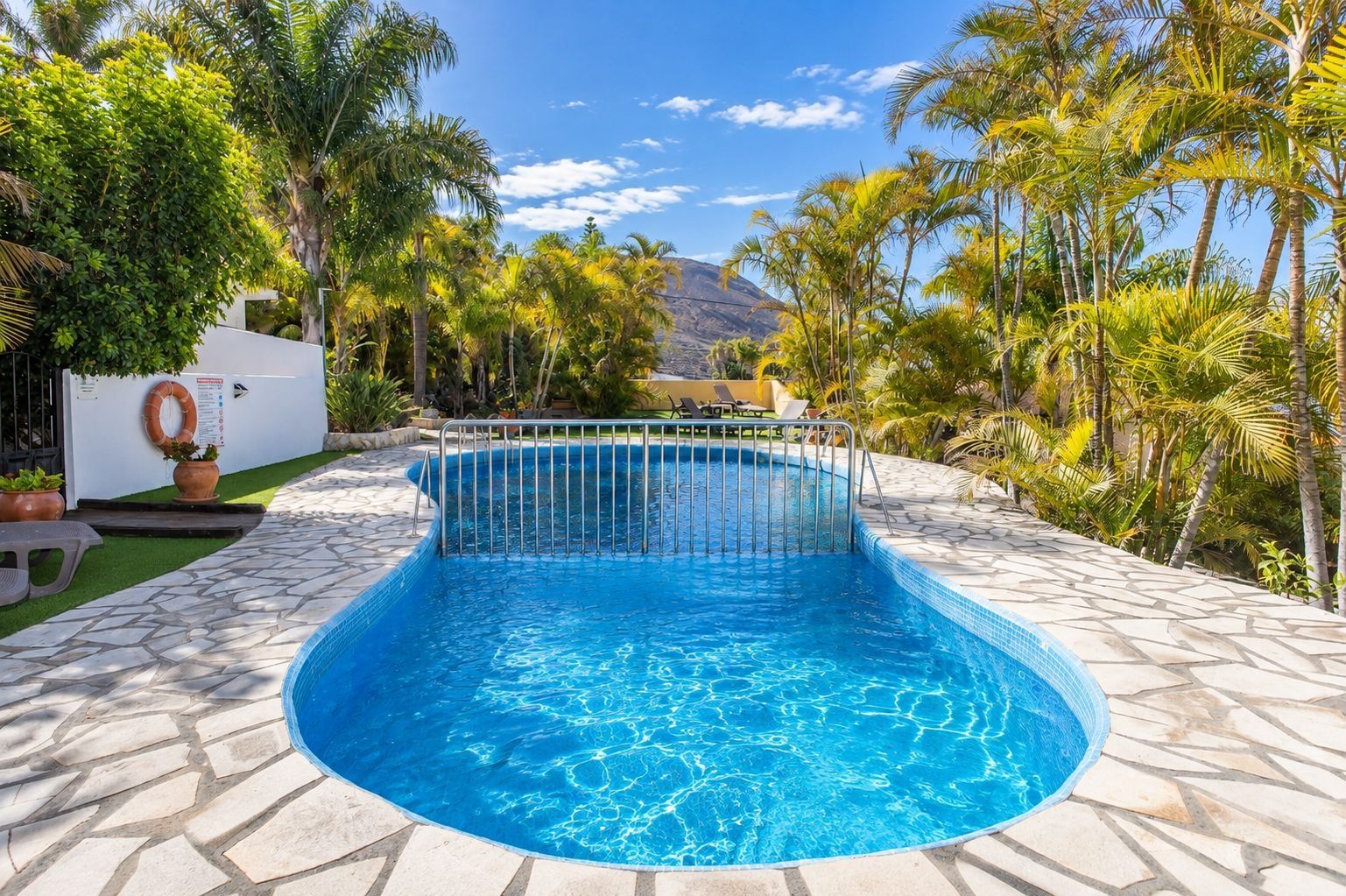 Ein Pool mit einer gefliesten Kante, umgeben von Palmen und einem Berg im Hintergrund.