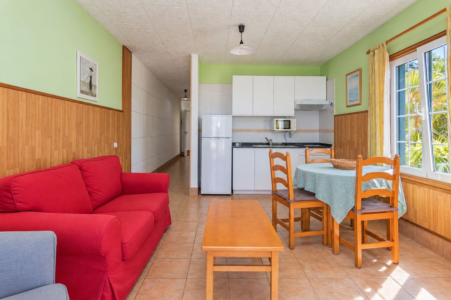 Un espacio habitable compacto con kitchenette, una zona de comedor con mesa y sillas, y un sofá rojo.
