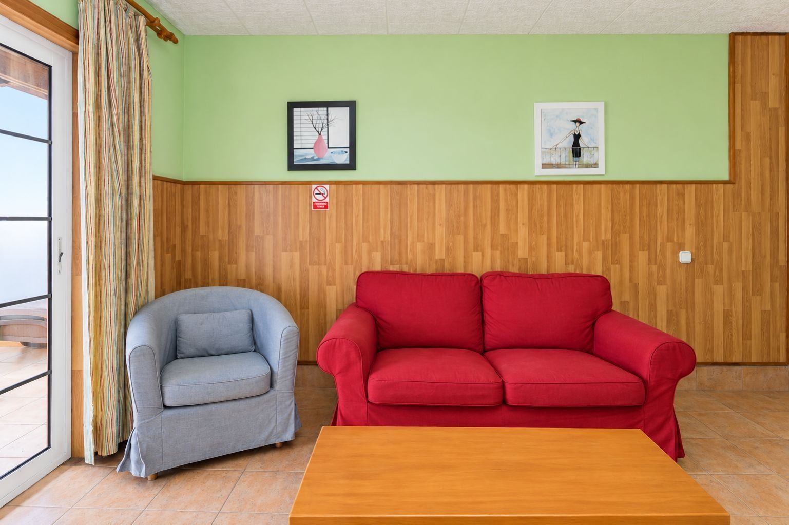 Ein Zimmer mit einem grauen Sessel, einem roten Sofa und einem Holztisch.