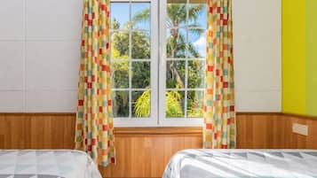Una habitación con dos camas, una ventana con cortinas, paredes de madera y vistas a zonas verdes.