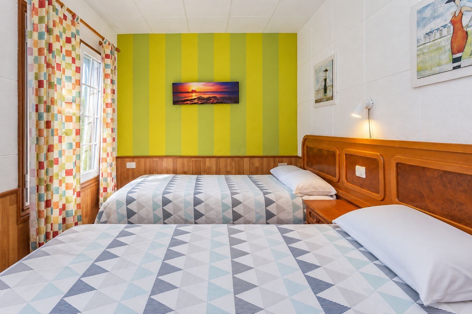 Ein Zimmer mit zwei Betten, einem großen Gemälde an der Wand und einem Fenster mit Vorhängen.