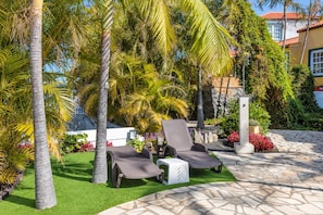 Un patio con dos sillones, una mesita y piso de baldosas de piedra.