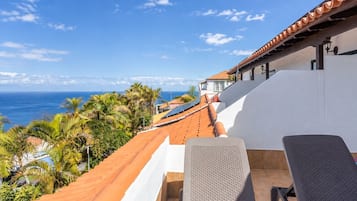 Una terraza con vistas al océano, palmeras y un edificio de techo rojo.