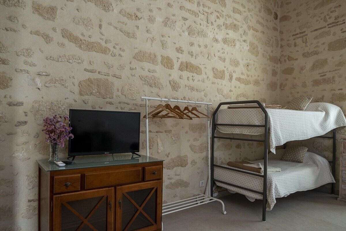 Une pièce avec un mur en pierre, un meuble en bois avec un téléviseur et un lit superposé.