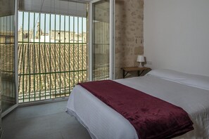 Ein Schlafzimmer mit Bett, Nachttisch, Lampe und Blick durch eine Schiebetür auf einen Außenbereich mit Metallzaun.
