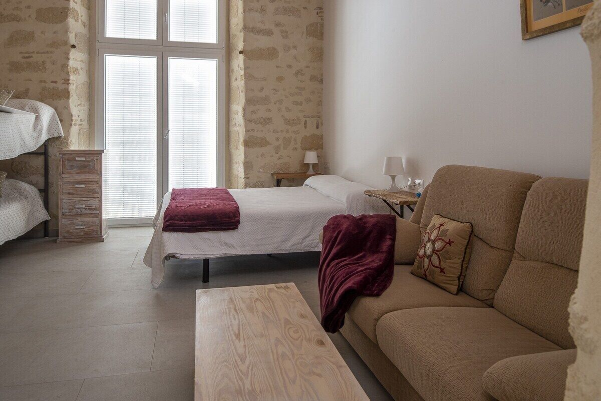 A bedroom with a bed, a sofa, a wooden table, and a dresser.