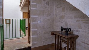 A room with a stone wall, a sewing machine on a wooden table, and a green gate leading to another room. - GuestReady - La Cruz 2D (El Puerto de Santa María)