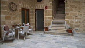 A stone-walled courtyard with a staircase, a table with chairs, and potted plants. - GuestReady - La Cruz 2D (El Puerto de Santa María)