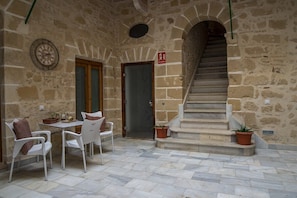 Ein Innenhof mit Steinwänden, einer Treppe, einem Tisch mit Stühlen und Topfpflanzen.