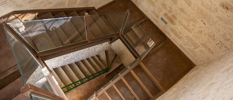 Escadaria em espiral com guarda-corpo de vidro e parede de pedra.