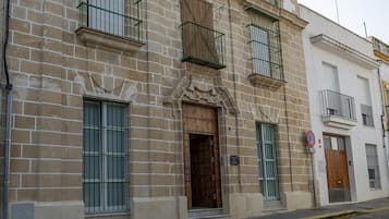 Un edificio con facciata tradizionale, caratterizzato da un ingresso centrale con porta in legno, diverse finestre con inferriate metalliche e un piccolo balcone al piano superiore.