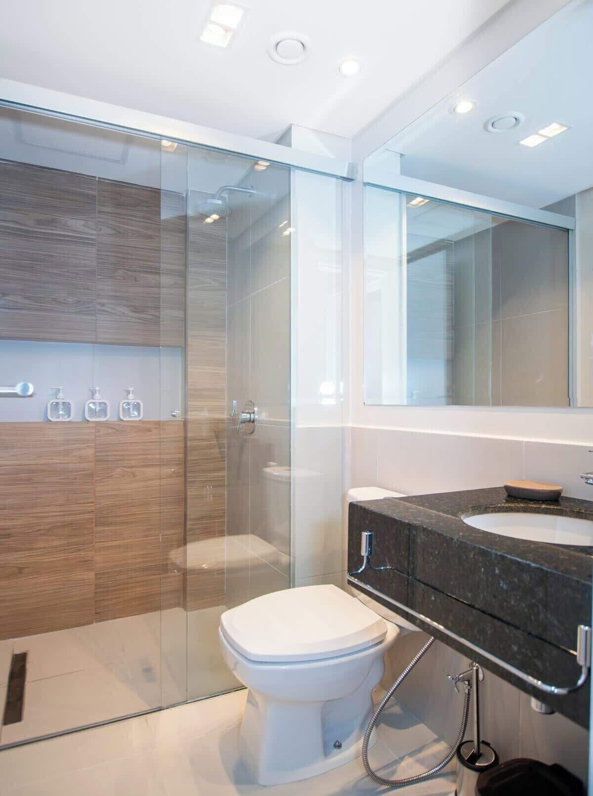 A modern bathroom with a glass shower enclosure, a white toilet, and a vanity with a dark countertop.