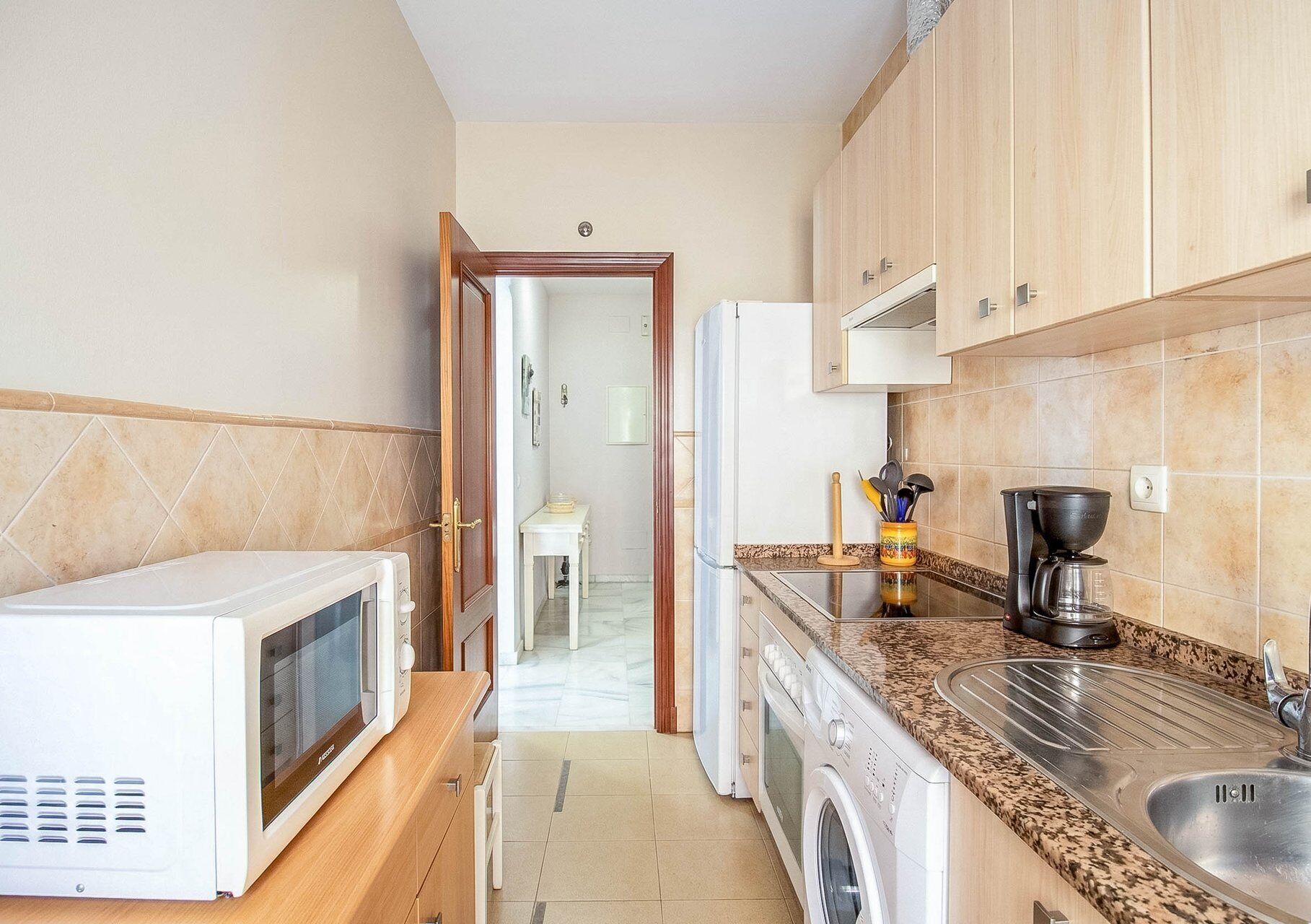 Una cocina compacta equipada con microondas, lavadora y cafetera.