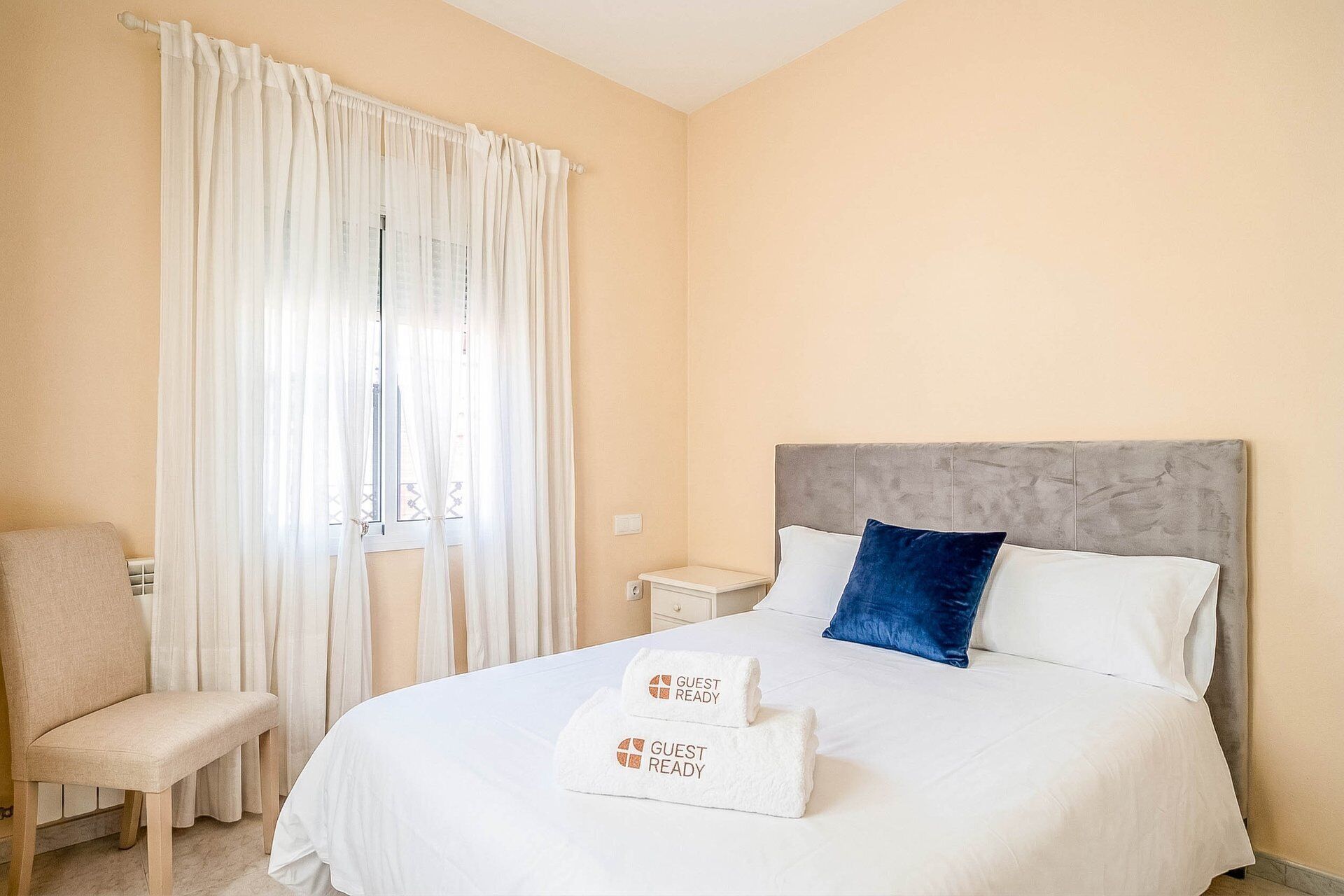 Une chambre d’hôtel avec un lit, une chaise, une table de chevet et une fenêtre avec des rideaux.