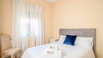 Une chambre d’hôtel avec un lit, une chaise, une table de chevet et une fenêtre avec des rideaux.