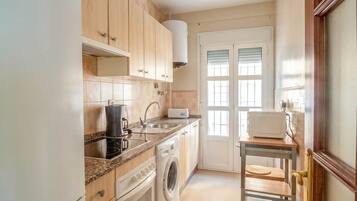Una cocina con armarios de madera, lavadora, microondas y una pequeña mesa con sillas.