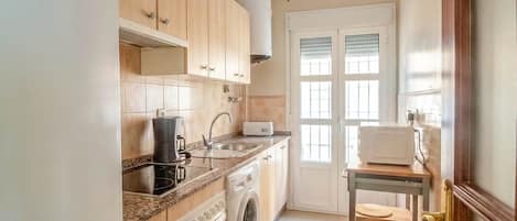 A kitchen with wooden cabinets, a washing machine, a microwave, and a small table with chairs.