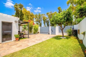 A modern outdoor patio with a tiled floor, a covered seating area, and a well-maintained lawn. - GuestReady - Valdelagrana Gus (El Puerto de Santa María)
