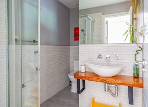 Une salle de bain moderne avec une douche à l’italienne en verre, un lavabo blanc doté d’un plan de travail en bois et un miroir agrémenté d’une plante.